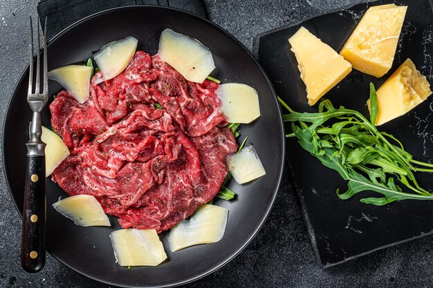Carpaccio-Salat mit marmoriertem Rindfleisch, Rucola und Parmesan. Schwarzer Hintergrund. Ansicht von oben.