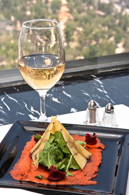 Carpaccio de salmón con queso gouda y rúcula servido con una copa de vino blanco bebida gastronómica