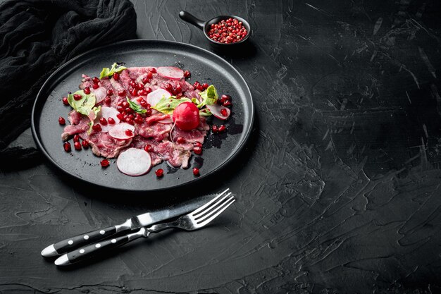 Carpaccio de ternera jaspeada, con rábano y granate, en placa, sobre fondo de piedra negra, con espacio para copiar texto