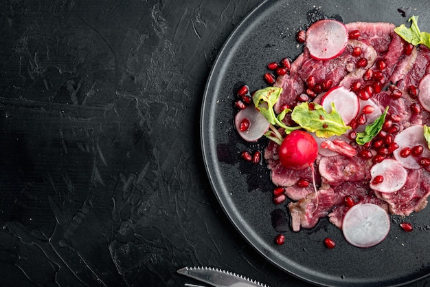 Carpaccio de ternera jaspeado, con rábano y granate, sobre plato, sobre piedra negra