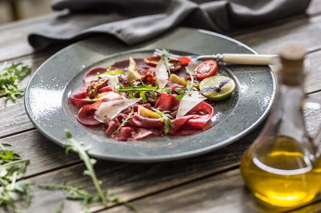 Carpaccio de ternera en plato con tomates secos alcachofas rúcula y parmesano.