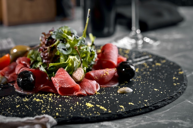 Carpaccio de ternera con rúcula en un plato negro, cocina tradicional italiana. Clave oscura, copie el espacio. Vista desde arriba