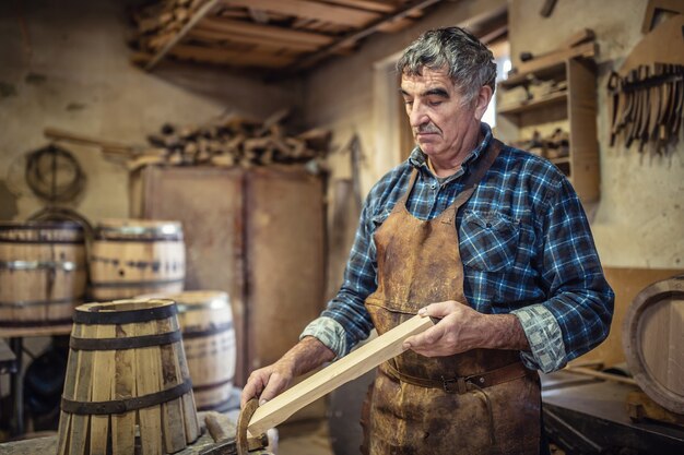 Carpenter evalúa la calidad de la madera que se utilizará en su taller para construir barriles de madera.