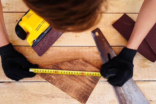 Carpenter midiendo la plancha de madera en el lugar de trabajo con guantes haciendo productos artesanales de madera