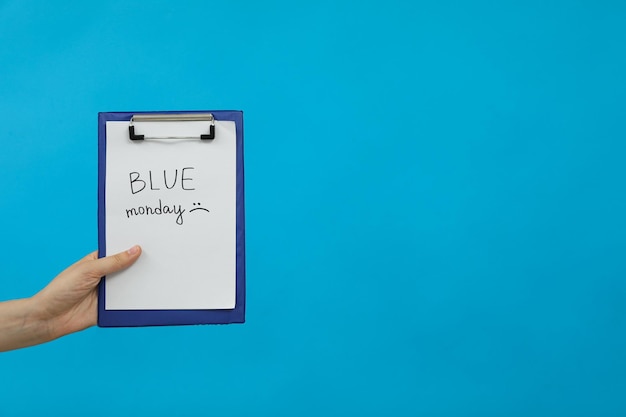 Carpeta y papel con texto Lunes azul en mano femenina sobre fondo azul espacio para texto