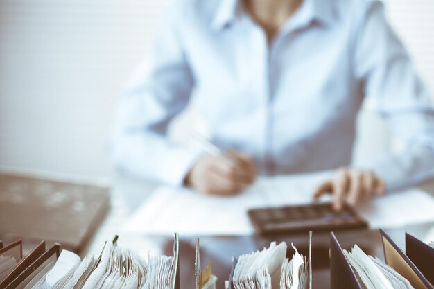 Carpetas de papeles a la espera de ser procesadas por una contadora o inspectora financiera, en primer plano. Retrato de negocios. Conceptos de auditoría o impuestos.