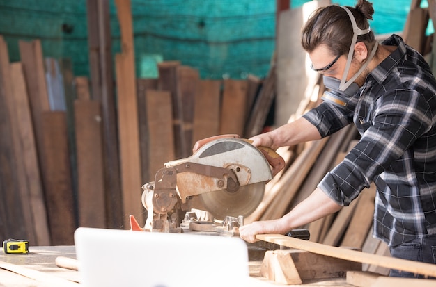 Carpinteiro caucasiano cortando madeira com serra circular criando móveis novos