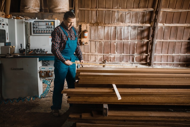 Carpinteiro com tábuas de medição de fitas métricas, máquina para trabalhar madeira, indústria madeireira, carpintaria. Processamento de madeira na fábrica, corte florestal em madeireira