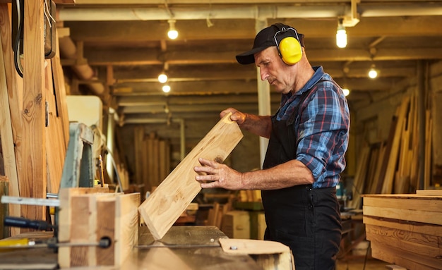 Carpinteiro sênior em uniforme trabalha em uma máquina de carpintaria na fabricação de carpintaria