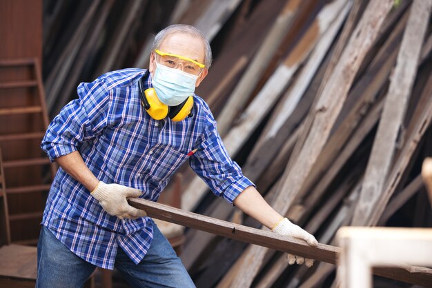 Carpinteiro, sênior, lixa cerca de madeira no local de trabalho usando uma ferramenta de trabalho