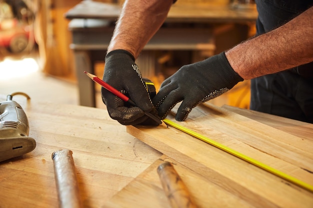 Carpinteiro trabalhando com uma prancha de marcação de madeira com um lápis e fazendo medições para cortar um pedaço de madeira para fazer um móvel em uma oficina de carpintaria vista de perto