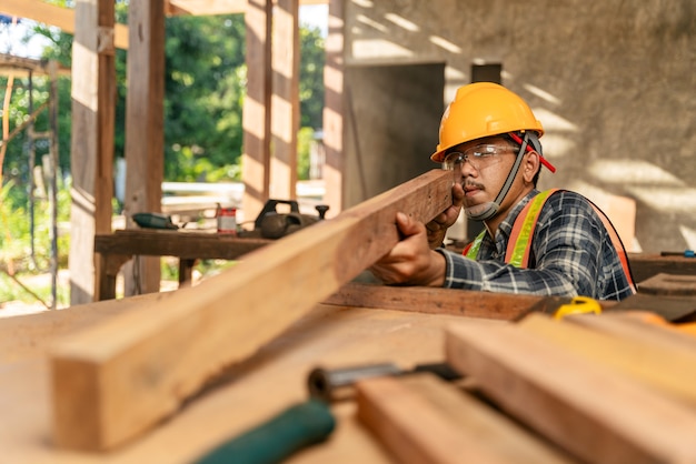 El carpintero asiático examina visualmente la precisión de la madera en el sitio de construcción.