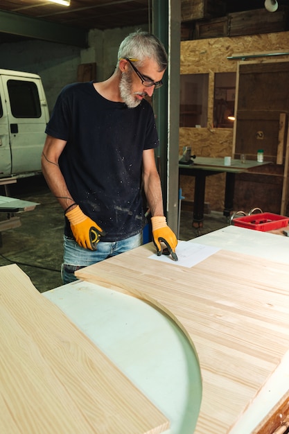 Carpintero comprobando las medidas de un trozo de madera en un plano