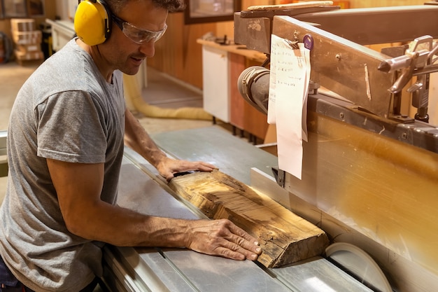 Carpintero cortando madera con una máquina con tapones para los oídos.