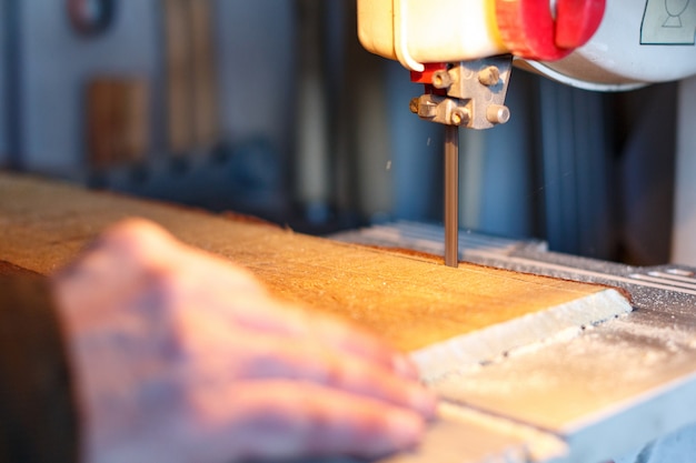 Carpintero cortando un trozo de madera con sierra de cinta en taller