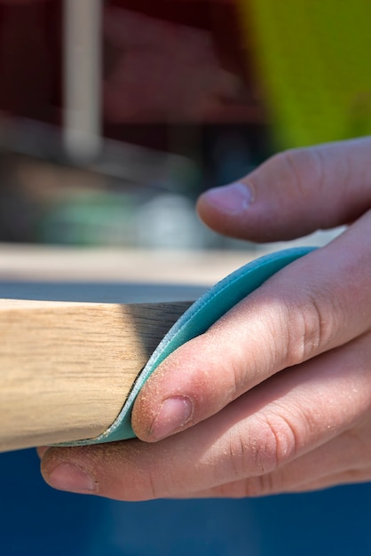Un carpintero está puliendo una tabla de madera con papel de lija. El proceso de fabricación de muebles de madera. Manos del primer plano maestro.