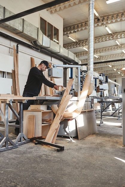 Foto carpintero experto en uniforme negro cortando un trozo de madera en su taller de carpintería