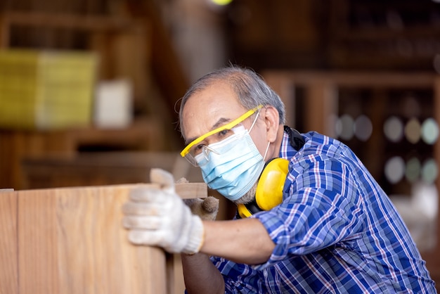 Carpintero, hombre Senior lijar la valla de madera en el lugar de trabajo con la herramienta de trabajo