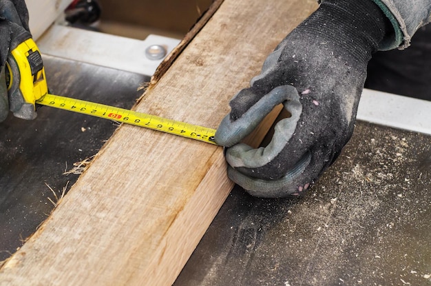 El carpintero mide el ancho de la tabla de madera con cinta métrica elástica
