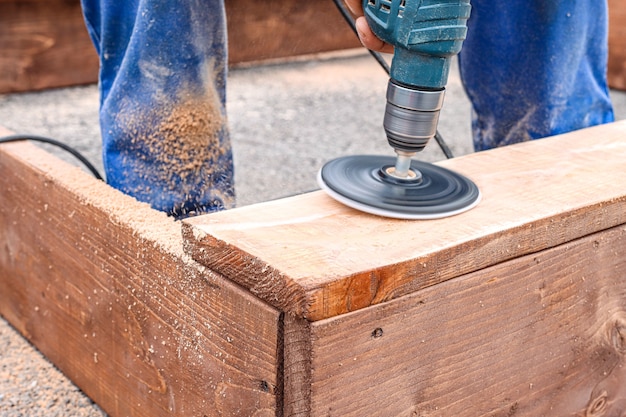 Un carpintero con un mono azul está cortando un trozo de madera con una lijadora en un área abierta