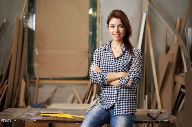 Carpintero de mujer feliz en camisa a cuadros con los brazos cruzados en el taller