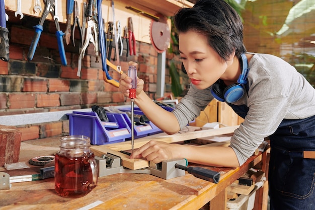 Carpintero mujer vietnamita concentrado con destornillador y tornillo de banco para unir tablas de madera