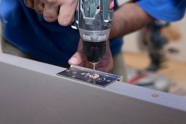 Un carpintero perfora un agujero en una tabla de madera con un taladro eléctrico