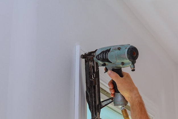 Carpintero con pistola de clavos para molduras en marcos de ventanas con la advertencia de que todas las herramientas eléctricas h