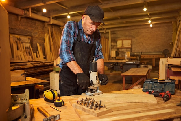 Carpintero profesional senior en trabajo uniforme de fresadora manual en el taller de carpintería