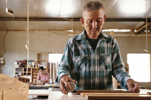 Carpintero senior concentrado midiendo tablones de madera con cinta métrica en su mesa de trabajo