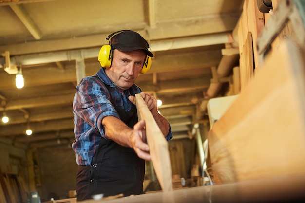 Carpintero senior en trabajos uniformes en una máquina de carpintería en la fabricación de carpintería