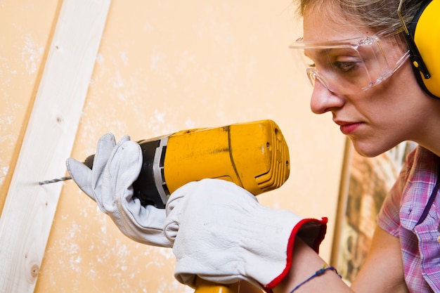 Carpintero de sexo femenino en el trabajo usando la perforadora de mano