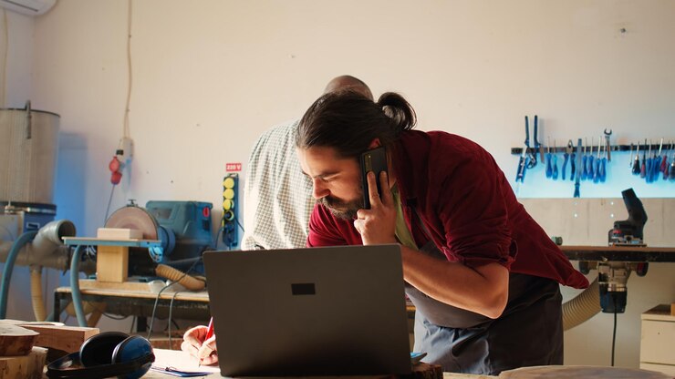 Foto carpintero en el taller de ensamblaje dibujando esquemas hablando en el teléfono inteligente
