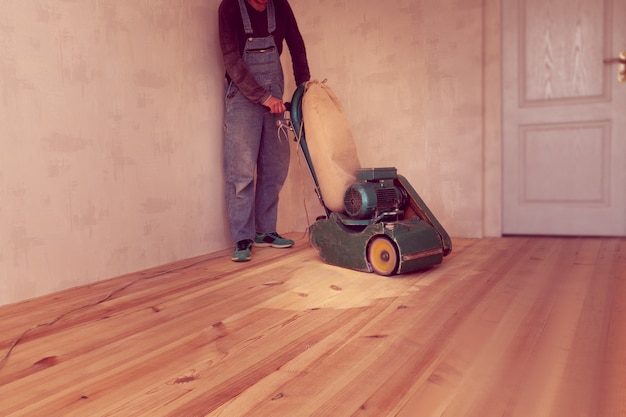 El carpintero trabaja con una máquina eléctrica de pulir madera en una habitación.