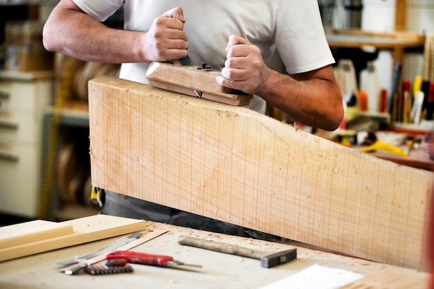 Carpintero trabajando con una cepilladora sobre un bloque de madera alisando la superficie en un primer plano de sus manos