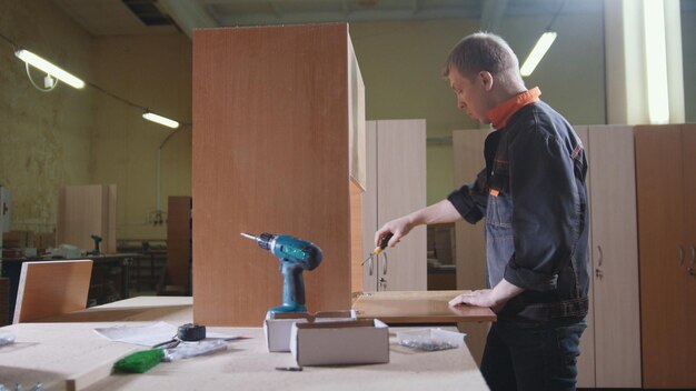 Carpintero trabajando con una grapadora industrial eléctrica en la fábrica, arreglando detalles de muebles, industria