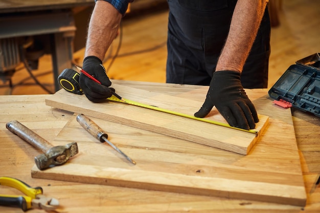 Carpintero trabajando con un tablón de marcado de madera con un lápiz y tomando medidas para cortar un trozo de madera para hacer un mueble en un taller de carpintería vista de cerca