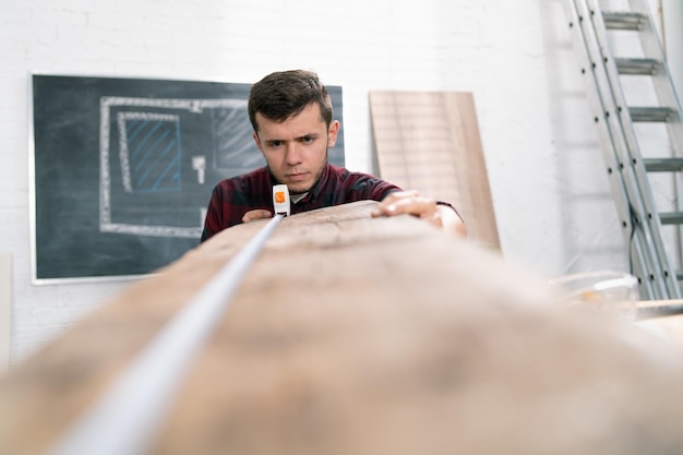 Carpintero en el trabajo, el hombre mide y marca el tablero de madera con una regla de metal y un lápiz