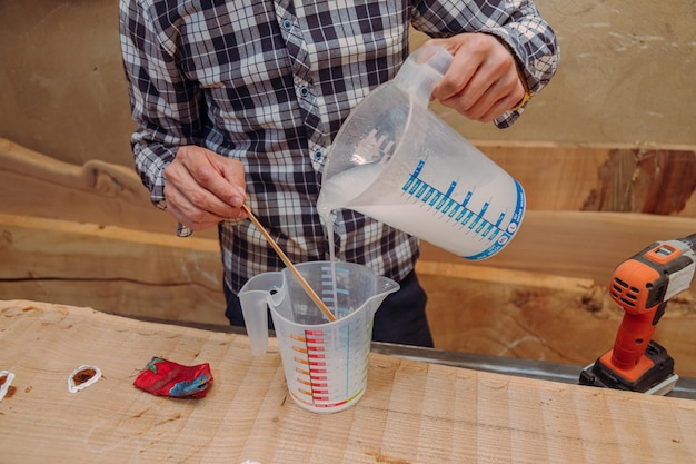 Foto carpintero vertiendo resina epoxi en un vaso de líquido en un taller