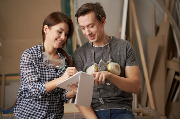 Carpinteros masculinos y femeninos sonrientes con el cuaderno en sus manos en el taller