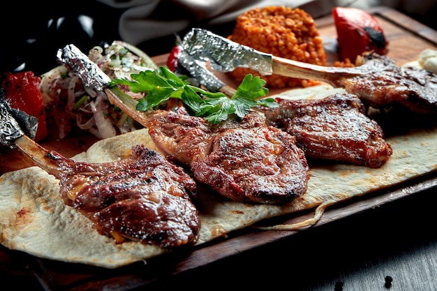 Carré de cordero cocido a la parrilla con pan de pita, bulgur y verduras a la plancha sobre tabla de madera. Shashlik turco.