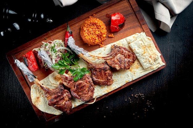 Carré de cordero cocido a la parrilla con pan de pita, bulgur y verduras a la plancha sobre tabla de madera. Shashlik turco.