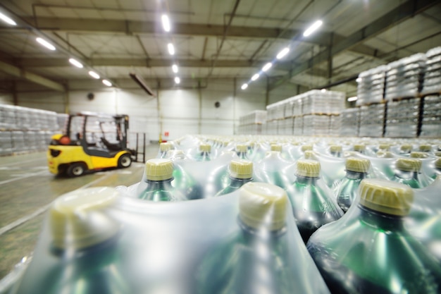 Carregador amarelo no fundo de um enorme armazém de alimentos industrial com garrafas pet de plástico com cerveja, água e bebidas.