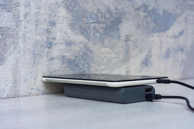 Foto carregamento de tablet com banco de potência em uma mesa de madeira cinza carregador portátil para dispositivos de carregamento