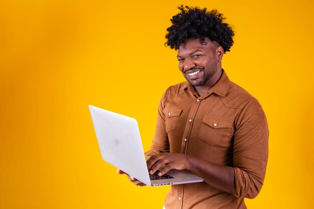 Carrera independiente Happy Black Guy usando computadora portátil sonriendo a la cámara de pie sobre fondo amarillo Foto de estudio Personas y gadgets Concepto de tecnologías de Internet y aprendizaje electrónico