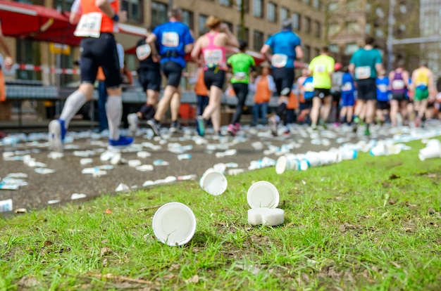 Carrera de maratón, pies de corredores y vasos de agua de plástico en la carretera cerca del punto de refrigerio, deporte, fitness y concepto de estilo de vida saludable