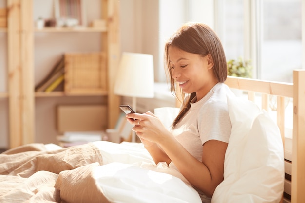 Carrera mezclada, mujer, usar teléfono inteligente, cama