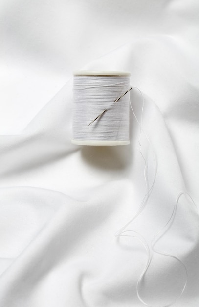 Carrete de hilo y aguja sobre algodón blanco
