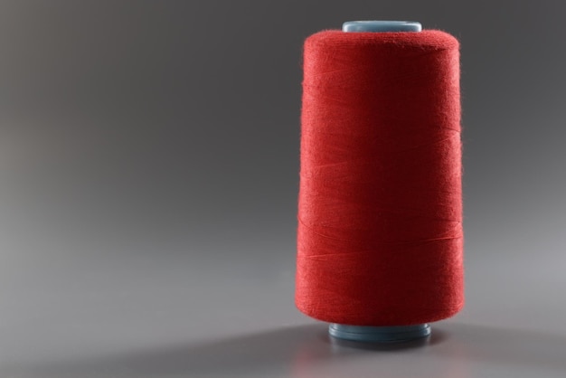 Carrete de hilo de color rojo sobre hilo de fondo gris para coser hilo brillante para confección