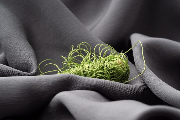 Carrete con hilos verdes sobre tela de seda gris primer plano de textura macro Lujoso fondo brillante y hermoso para coser Adaptación del concepto del taller Tejidos naturales de alta moda